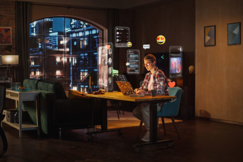 Frau sitzt bei Nacht vor dem Computer. Man sieht viele Programmfenster mit Social Media Inhalten, die Sie umzingeln.